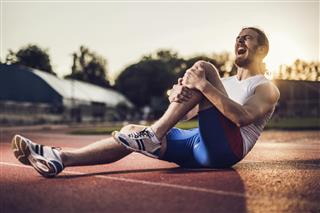 Injured male athlete screaming in pain at sunset