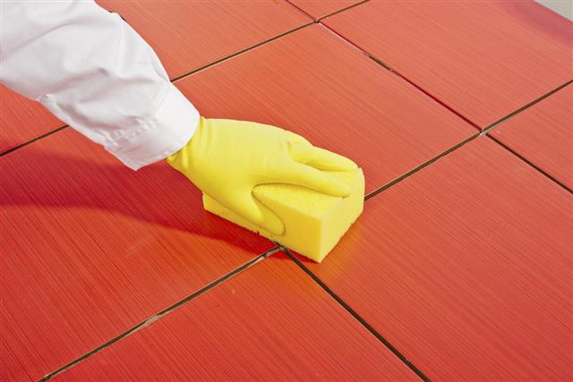 Hand with yellow gloves and sponge cleans red tiles