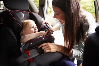 Mother securing infant daughter in car seat