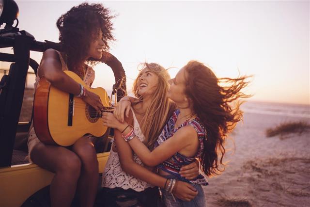 Afro girl playing guitar for her friends at sunset