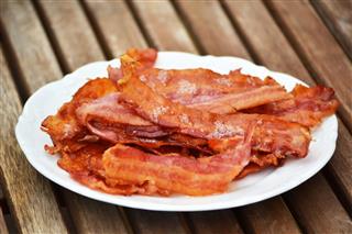 Pile of crispy bacon on a white plate on a wooden surface