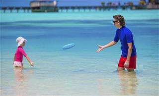 Father and little daughter playing with flying disk at beach