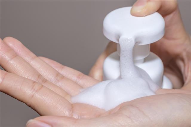 Female hands applying liquid soap close up on cream backgroud
