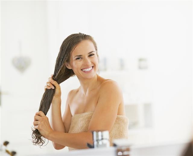 Happy young woman applying hair mask in bathroom