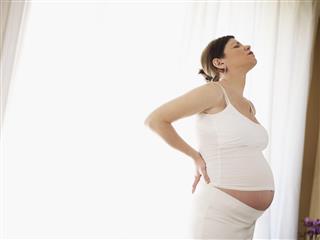 Pregnant woman holding back in front of white curtain