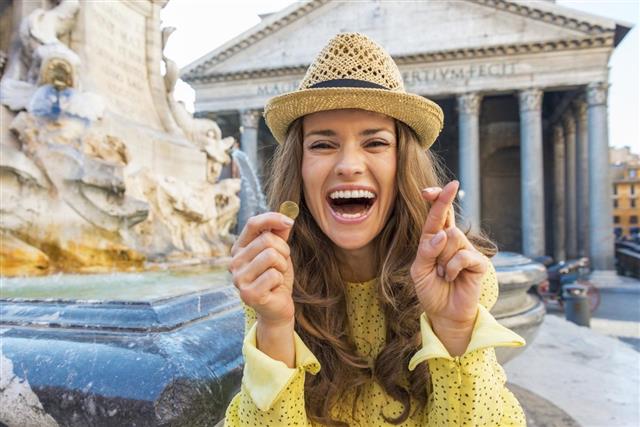Woman with crossed fingers and coin near fountain in rome