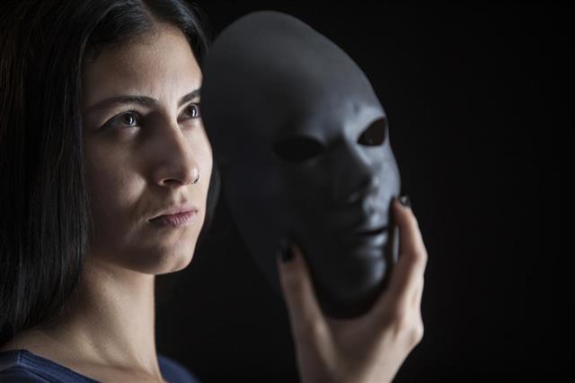 Young woman peeking behind mask in dark