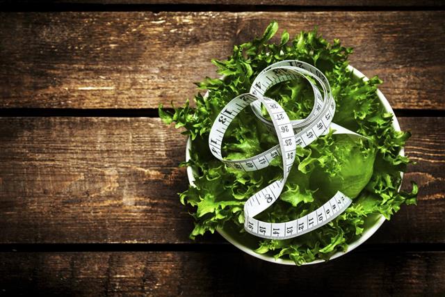Salad with fitness measuring tape over wooden background.