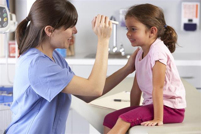 A smiling doctor examines a child's eyes in her office