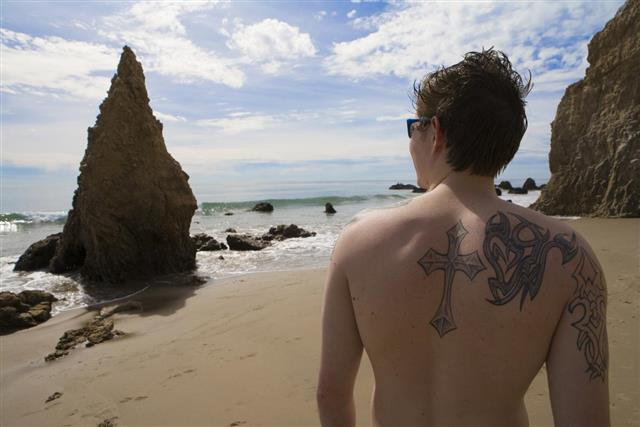 Young man with tattoos looks out to ocean
