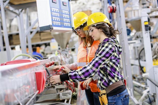 Two women working in a factory and wearing hardhats