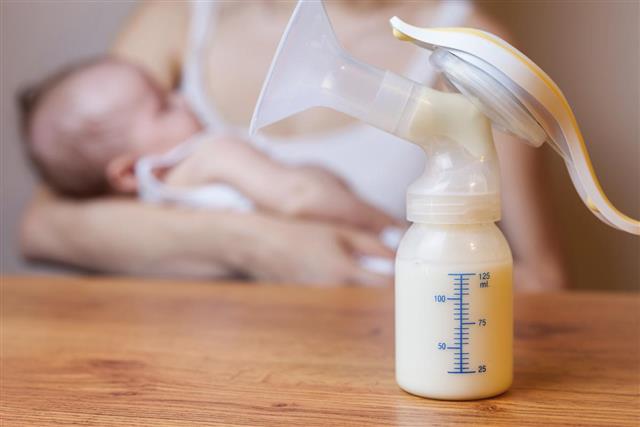 Manual breast pump with milk mother and baby at background