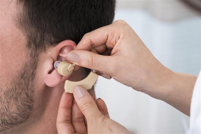 Hands Inserting A Hearing Aid Into A Man's Ear