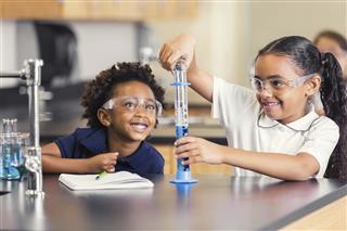 Cute elementary students smiling while doing science experiment in class