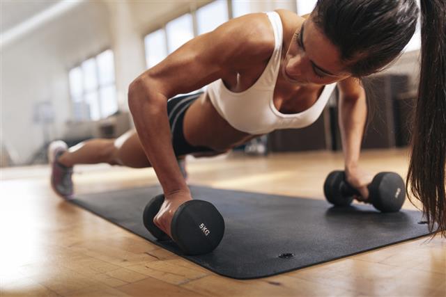 Gym woman doing pushups on dumbbells