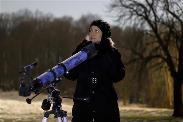 Woman with telescope under winter night sky