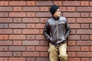 Asian Man in a Brown Jacket Leans Against the Wall