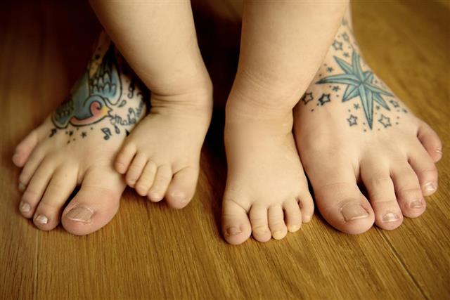 Adult tattooed feet with baby feet in between