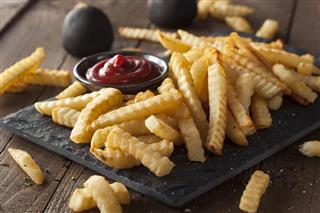 A plate of unhealthy baked crinkle French fries and ketchup