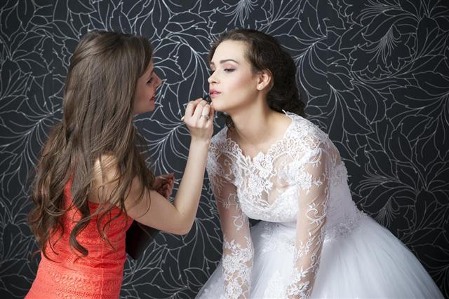 Makeup artist applies lipstick to bride